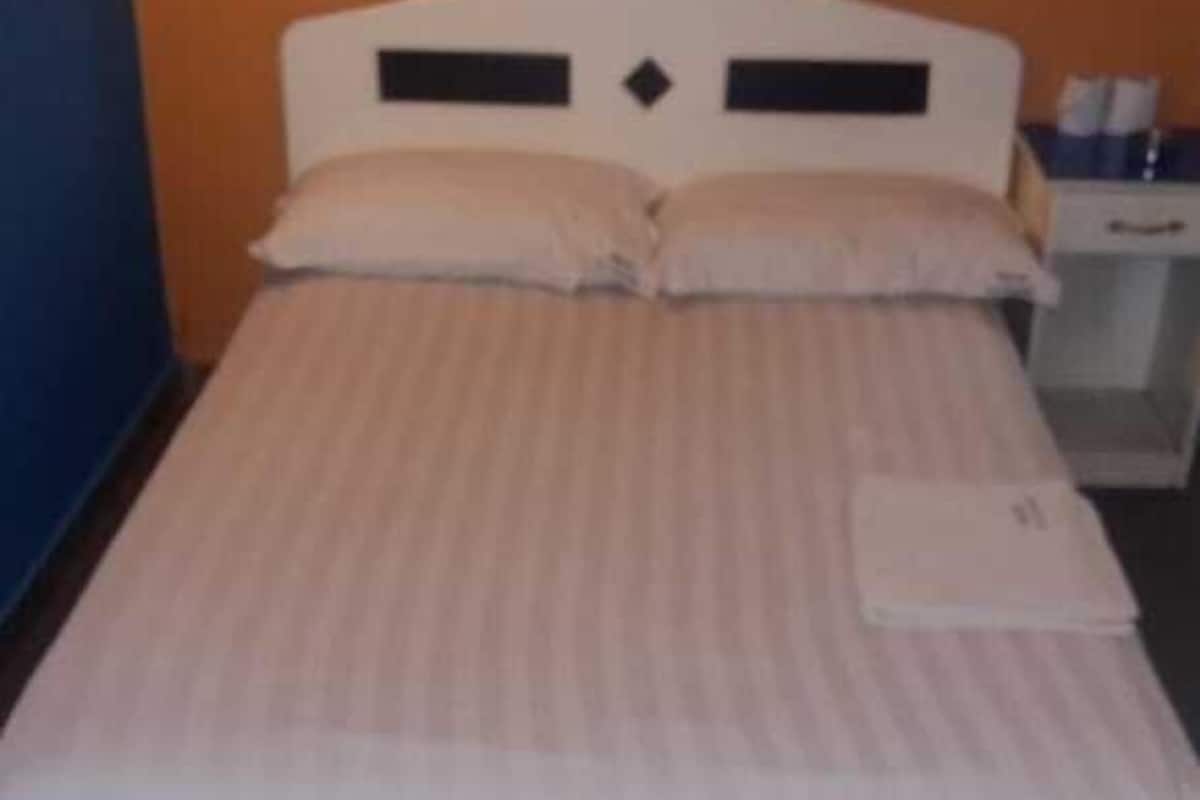 A single bed with a white headboard and a striped mattress in a room with an orange wall.