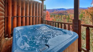 Un jacuzzi en una terraza de madera con vistas al follaje otoñal y montañas.