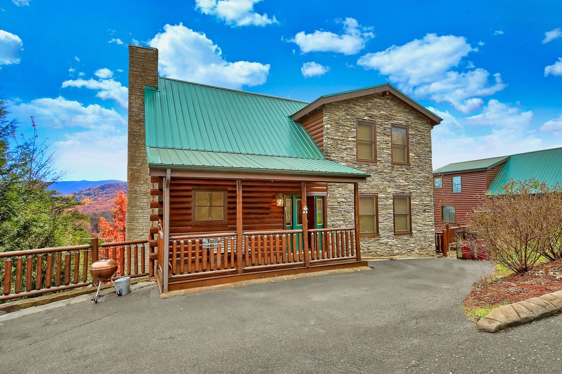 A log cabin with a stone tower, a porch with a railing, and a view of the mountains.