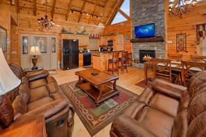 A log cabin interior with a living room, dining area, kitchen, fireplace, and a TV mounted on the wall.