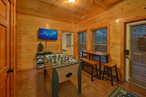 A cozy room with wooden walls, a foosball table, a TV, and a bar area.