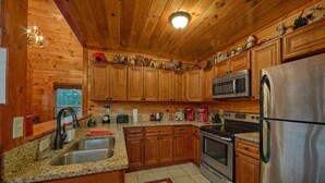 A wooden cabin-style kitchen with granite countertops, stainless steel appliances, and holiday decorations. - Reindeer Bay: Private Pool, Amazing Views, Games (PIgeon Forge)
