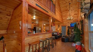 A cozy log cabin interior with a bar area, seating, and a Christmas tree. - Reindeer Bay: Private Pool, Amazing Views, Games (PIgeon Forge)