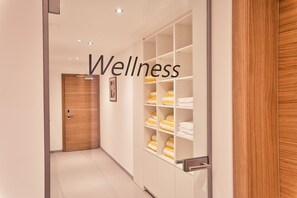 A hallway with a wooden door, a white wall, and a shelving unit with towels. - Rössle Appartements (Fontanella)