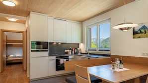 Une cuisine moderne avec des meubles blancs, un four encastré et un coin repas comprenant une table et des chaises en bois.