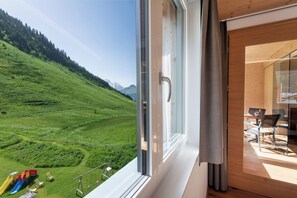 A room with a large window overlooking a green valley and mountains. - Rössle Appartements (Fontanella)