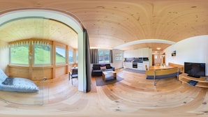 Un intérieur moderne avec un plafond en bois aux lignes courbes, un espace de vie comprenant un canapé et une table basse, une cuisine avec des meubles blancs et une grande fenêtre donnant sur un paysage verdoyant.