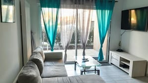 A living room with a sofa, a glass coffee table, a flat-screen TV, and teal curtains. - Flat for 4 , 150m from the beach in Sion (Saint-Hilaire-de-Riez)