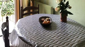 A dining area with a round table covered by a striped tablecloth, a bowl of fruit, and a potted plant with flowers. - Large terraced house, with garden, in quiet area (Dijon)