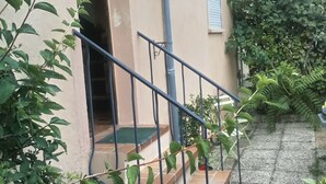 A house with a staircase leading to a door, surrounded by potted plants and a small garden area. - Large terraced house, with garden, in quiet area (Dijon)