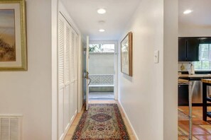 A hallway with a patterned rug, a door with louvered shutters, a framed picture on the wall, and a kitchen area with a dishwasher and cabinets. - Spacious Garden Unit on Historic Jones Street! (Savannah)