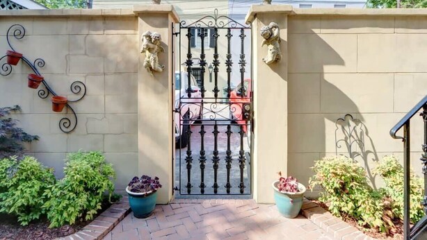 A gated entrance with a wrought iron gate, two stone lion statues, and potted plants. - Spacious Garden Unit on Historic Jones Street! (Savannah)