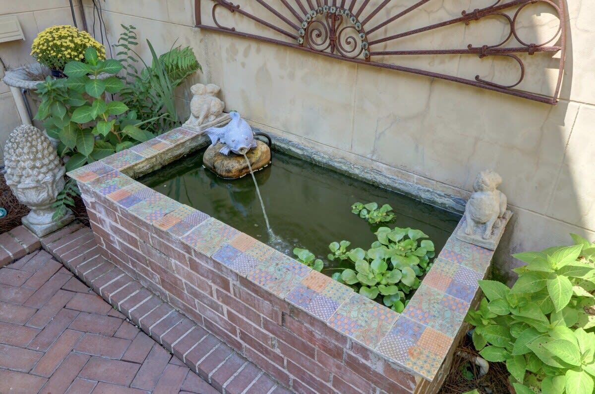 Un pequeño estanque decorativo con borde de azulejos, rodeado de plantas y esculturas de piedra.