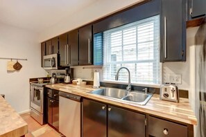 A modern kitchen with dark cabinets, stainless steel appliances, a double sink, and a window with blinds. - Spacious Garden Unit on Historic Jones Street! (Savannah)