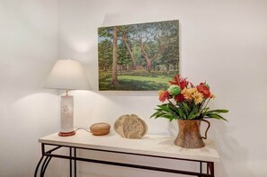 A beautifully styled table features a textured lamp, woven basket, and decorative piece, complemented by a rustic pitcher and a framed landscape painting.