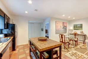 A modern kitchen with a wooden table and chairs, a refrigerator, and a tiled floor. - Spacious Garden Unit on Historic Jones Street! (Savannah)