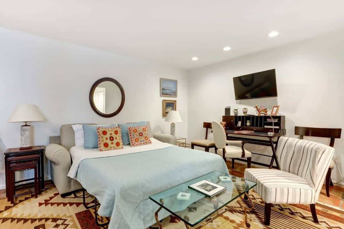 A bedroom with a bed, a desk, a chair, a TV, and a mirror.