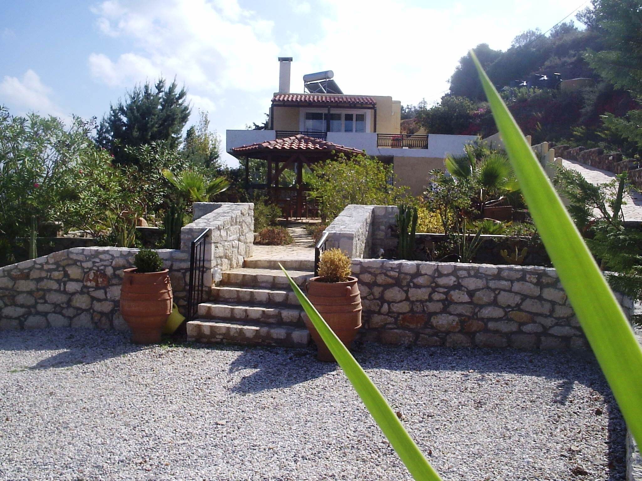 A stone staircase leading to a house with a tiled roof, surrounded by gravel and potted plants.