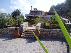 Un escalier en pierre mène à une maison dont le toit est recouvert de tuiles, et qui est entourée de gravier et de plantes en pot.