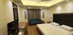 Habitación de hotel con cama, escritorio con computadora, silla, televisión y ventilador de techo.