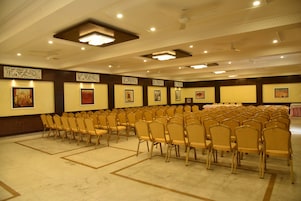 Un salón de conferencias con filas de sillas, luces en el techo y cuadros en las paredes.