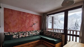 Une pièce chaleureuse avec un banc en bois et une table, un mur rouge à la texture intéressante et une fenêtre donnant sur un paysage enneigé.