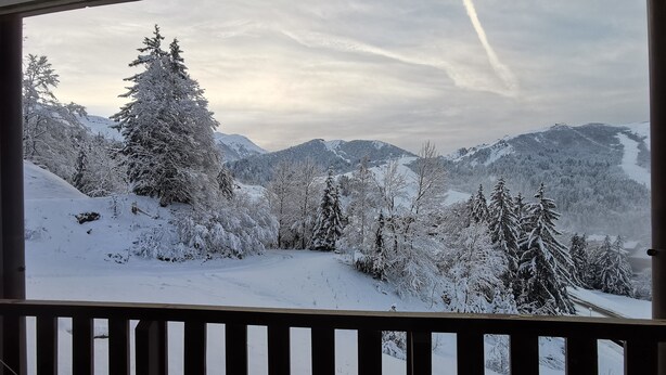 Un paysage de montagne enneigé, vu à travers une fenêtre équipée de stores verticaux.