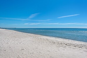 A beach with a pier extending into the water, clear skies, and calm sea.