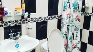 Baño con lavamanos blanco, inodoro y cortina de ducha con motivos florales.