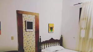 Una habitación con dos camas individuales, una puerta de madera, un estante pequeño sujeto a la pared y una cortina.