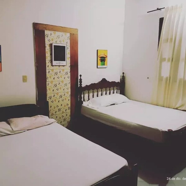 A room with two single beds, a wooden door, a small wall-mounted shelf, and a curtain.