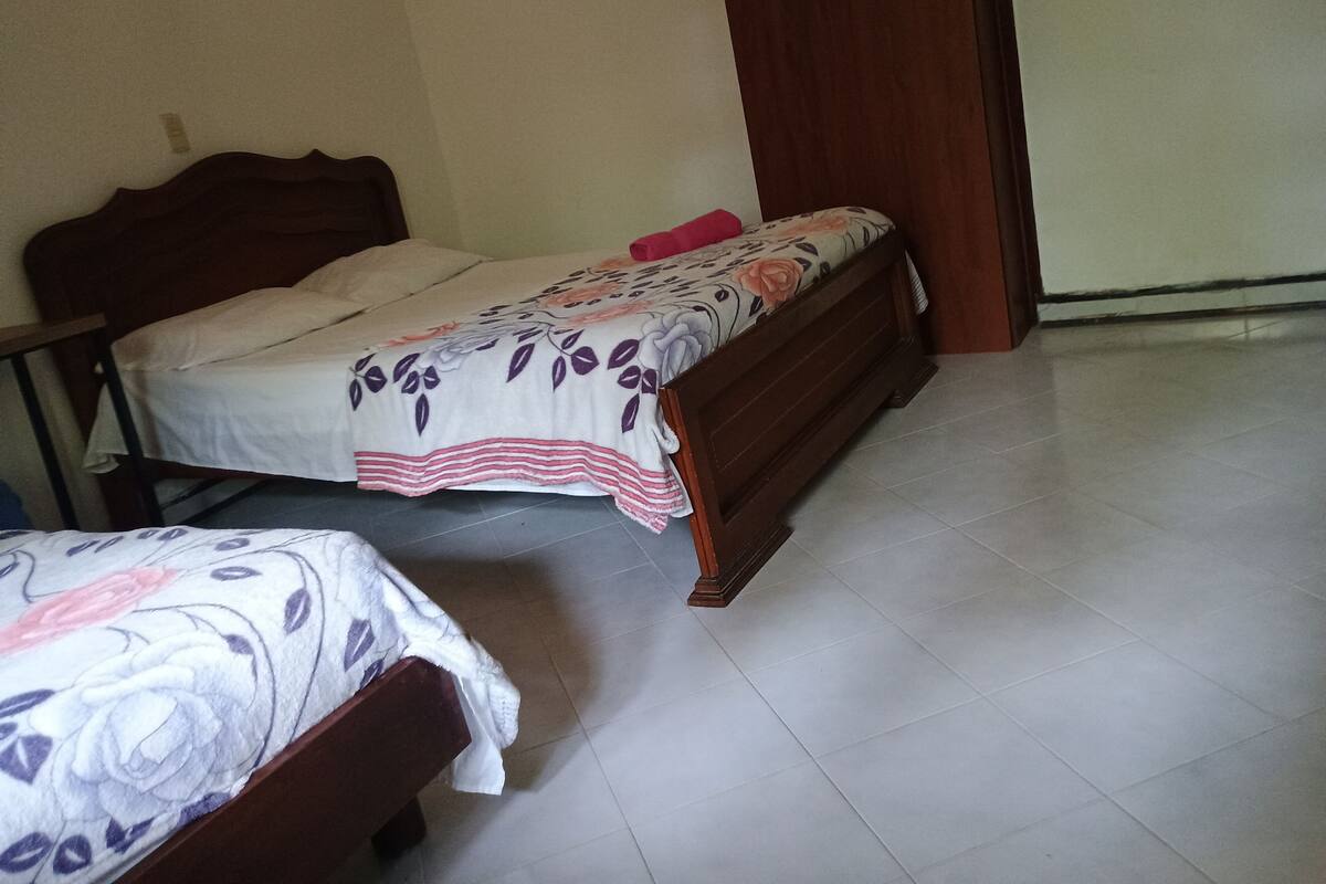A room with two wooden beds, one with a floral bedspread and the other with a plain one.