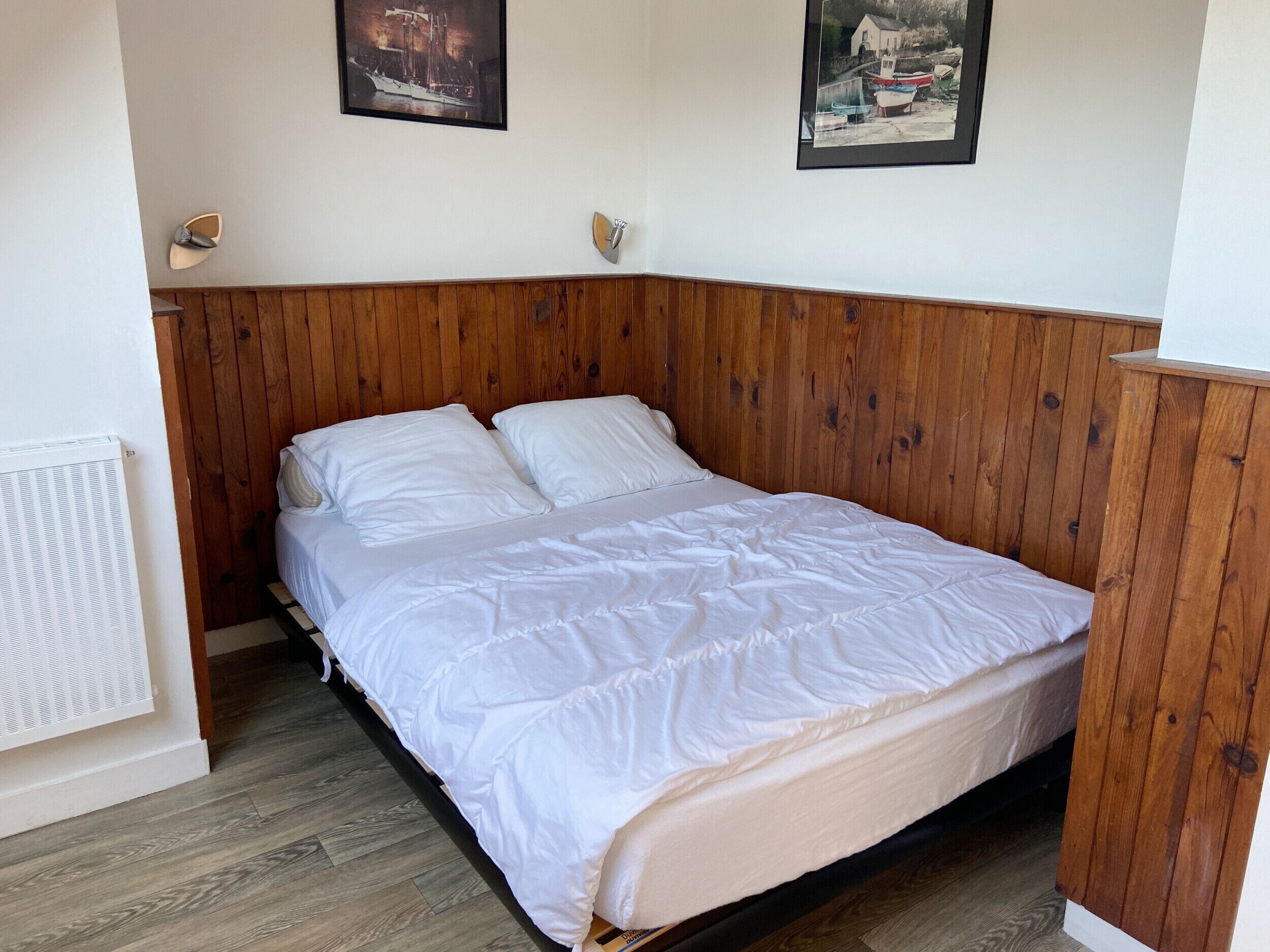 A single bed with white bedding in a room with wooden paneling on the walls and a radiator on the left.