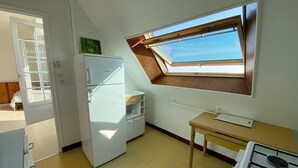 A compact kitchen with a built-in refrigerator, a small table, and a window with a view. - MOUETTES 3 - Apartment with sea view between Carnac and Trinité-sur-Mer - T356 (La Trinité-sur-Mer)