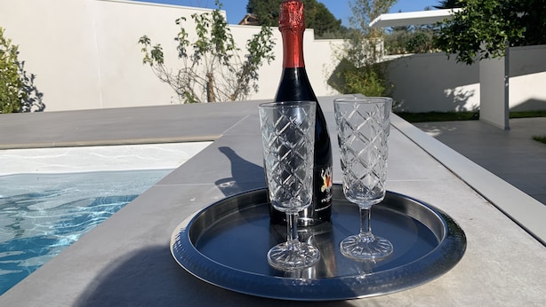 Una botella de vino y dos copas sobre una bandeja junto a una piscina.