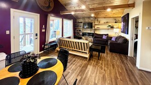 Een gezellige woonkamer met een open haard, houten plafond en een eethoek met een tafel en stoelen.