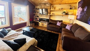 Een gezellige woonkamer met houten balken, een open haard, een televisie en een boekenkast.
