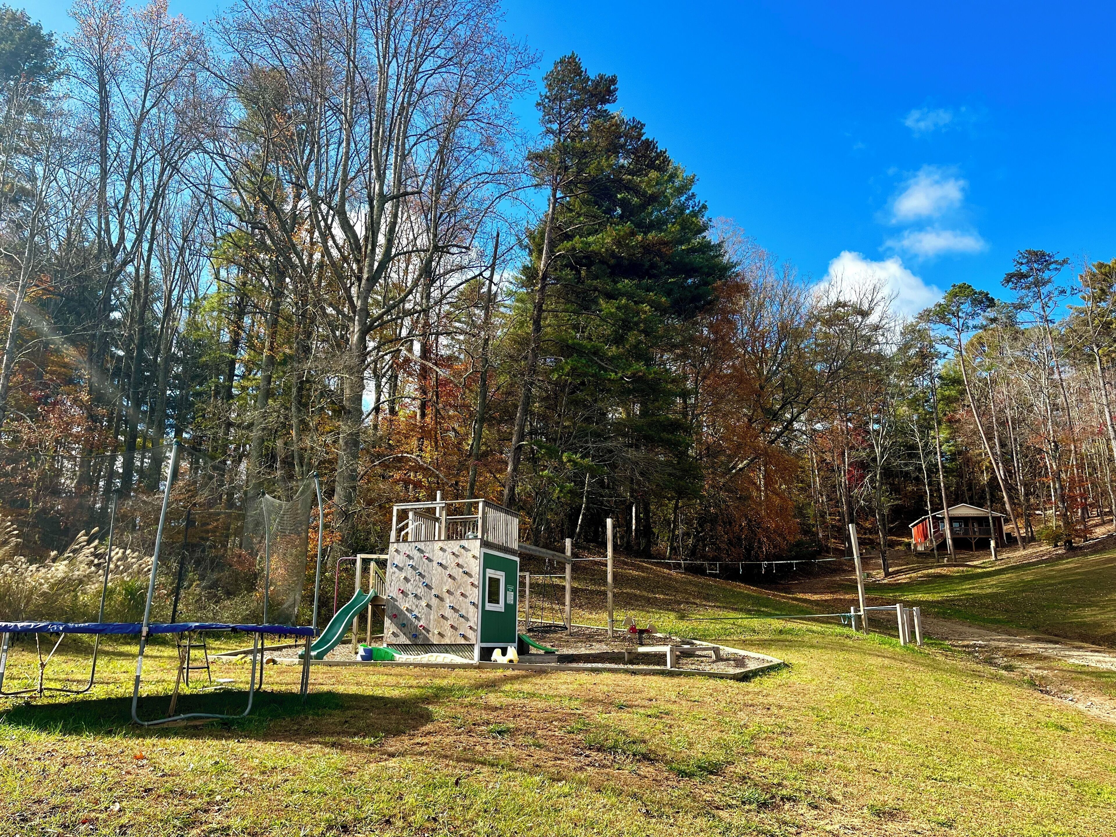 A playground with climbing structures and a slide, surrounded by trees and a grassy area.