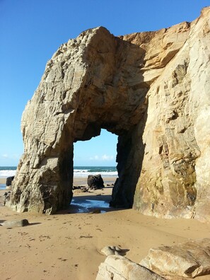 A natural rock arch formation on a beach with clear skies.