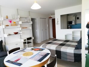 Un ambiente compatto con zona pranzo, angolo cottura e un letto con coperta a quadretti.