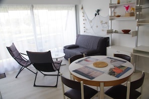 Un soggiorno moderno con un divano grigio, un tavolo da pranzo rotondo con sedie e un mobile bianco con ripiani.