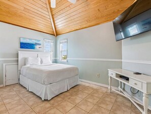 A bedroom with a bed, a desk, and a television on the wall.