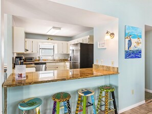 A modern kitchen with white cabinets, a stainless steel refrigerator, a granite countertop, and a bar stool with a colorful design.