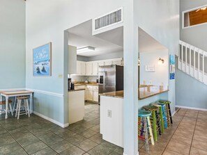 A modern kitchen with white cabinets, a stainless steel refrigerator, and a dining area with a table and stools.