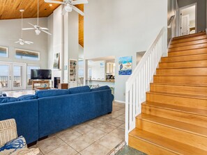 A spacious living area with a large blue sofa, a wooden staircase, and a view of the ocean through large windows.