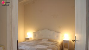 A bedroom with a bed, two bedside tables with lamps, and a door. - Hibiscus apartment | Garda Lake & Golf (Padenghe Sul Garda)