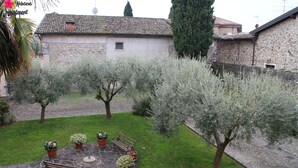 A courtyard with a stone bench, potted plants, and a stone pathway. - Hibiscus apartment | Garda Lake & Golf (Padenghe Sul Garda)
