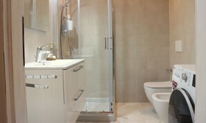 Un baño moderno con ducha de vidrio, inodoro y lavadora.