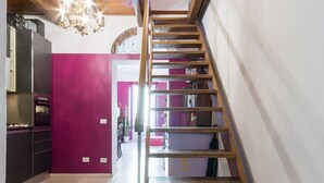 Een houten trap in een moderne keuken met een roze muur en een kroonluchter.