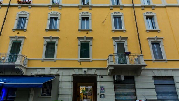 Un edificio giallo con molte finestre e balconi, un ingresso ben visibile e un'auto parcheggiata davanti.